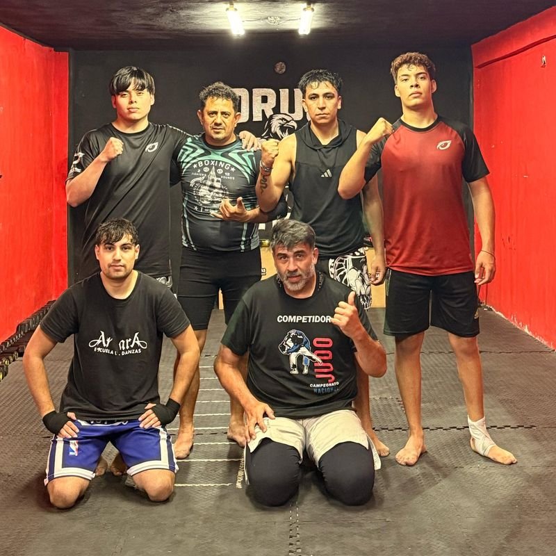 Seis integrantes del equipo de ORUS posando con el puño en alto frente al logo del gimnasio